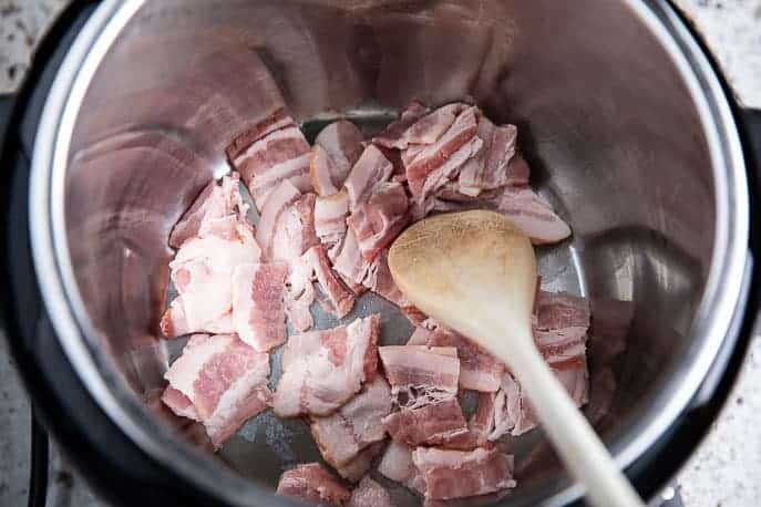Instant Pot with raw bacon and a wooden spoon