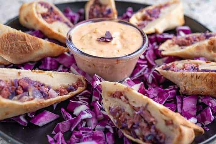 Air Fried Reuben Egg Rolls with Healthy Thousand Island Dressing on a black plate with red cabbage