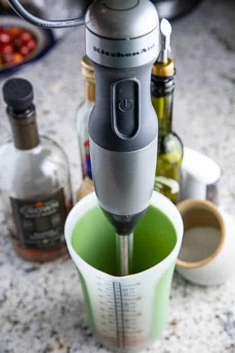 Immersion blender in a cup with ingredients around on a granite counter