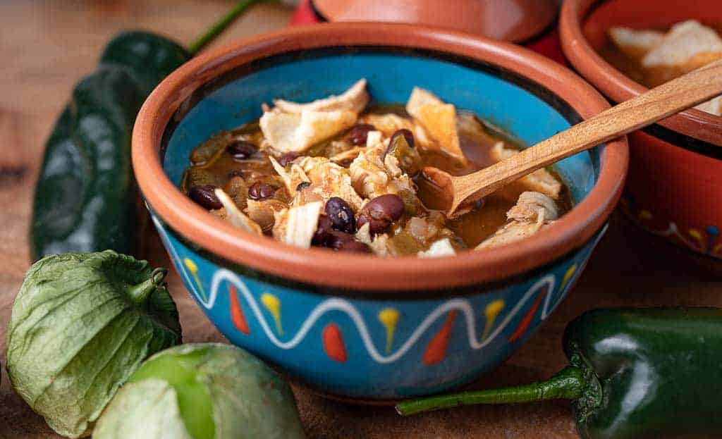 Healthy Soup Recipes: Mexican bowl with Chipotle Chicken Soup, wooden spoon, tomatillos and peppers