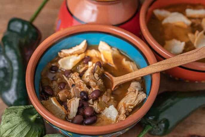 2 bowls of chicken tortilla soup with tomatillos and poblanos on a wooden board