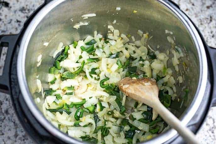 Onions and peppers cooking in an Instant Pot with wooden sppon