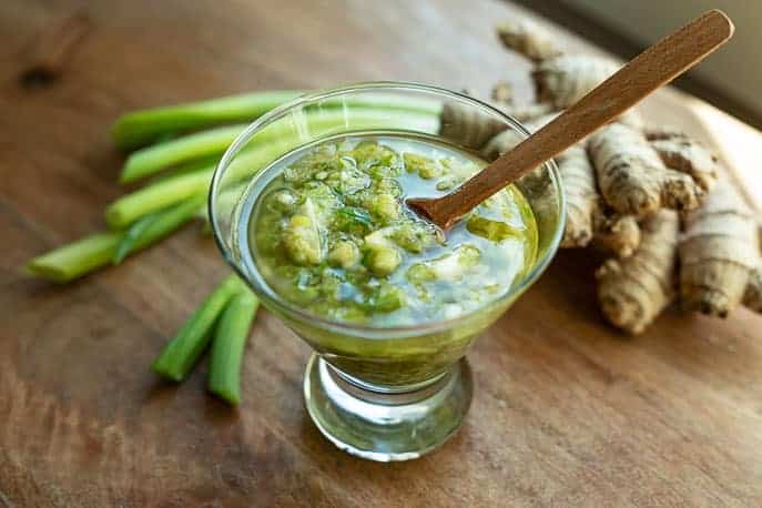 Easy Ginger Scallion Sauce in a glass dish with green onions and ginger on a wooden board