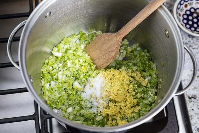 Green onions, ginger, garlic, salt in a large metal pot with wooden spoon.