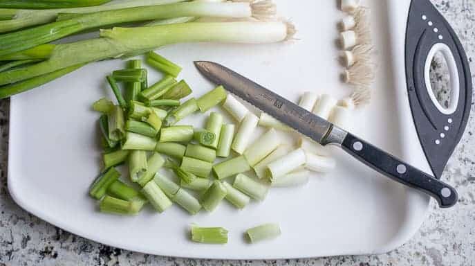 Green onions on a white cutting board with knife