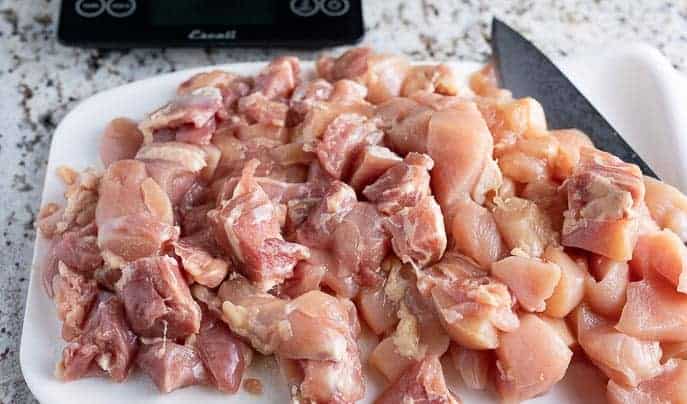 raw chicken on a white cutting board with knife, scale in the background on a granite counter top