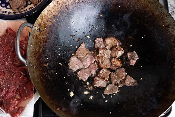 Beef pieces in a wok with raw meat next to it
