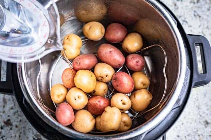 Potatoes in the Instant Pot on a rack, measuring cup of water being poured in