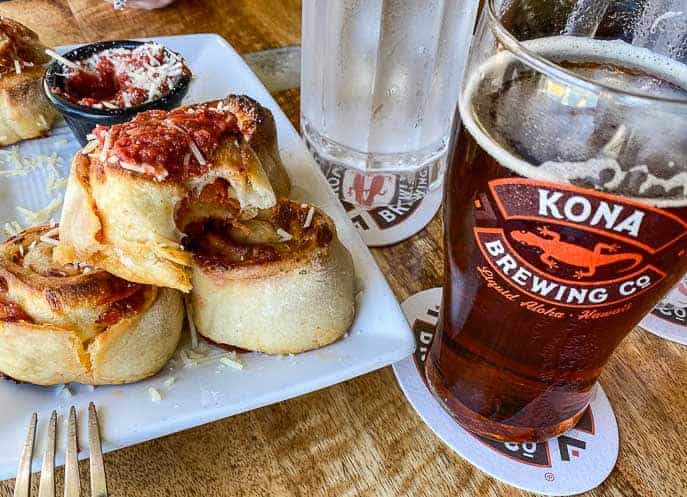 Kona brewing company pepperoni rolls on a white plate with fork, Kona beer and water in the background