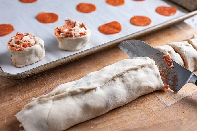 pepperoni roll with slices and knife, baking sheet with rolls in the background