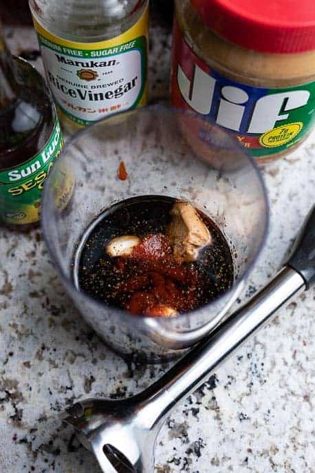 Plastic container with ingredients for homemade hoisin sauce and immersion blender on a granite countertop