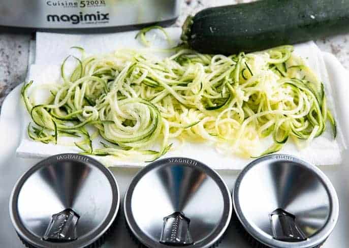 Magimix food processor, paper towel with spiralized zucchini, 3 different spiralizer blades and a zucchini