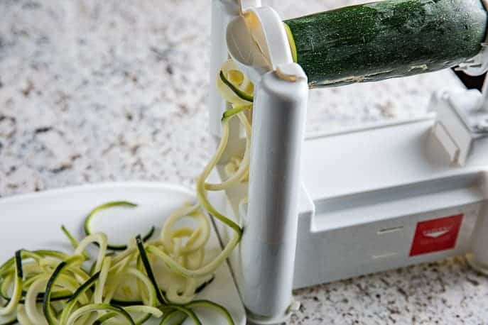 Zoodles hanging off the Paderno spiralizer onto a cutting board on a granite counter top