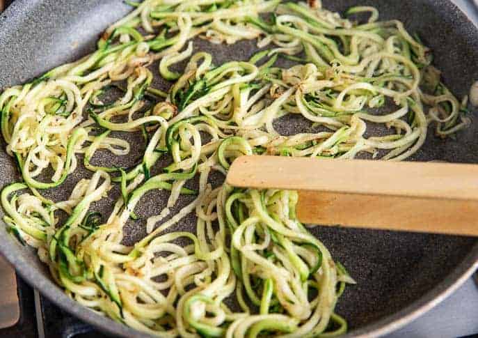 Zoodles in a non stick pan with wooden tongs