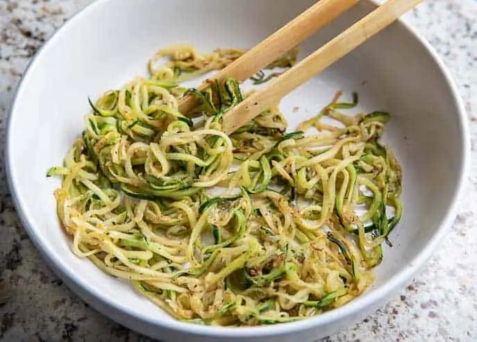 Zoodles in a white bowl with wooden tongs.