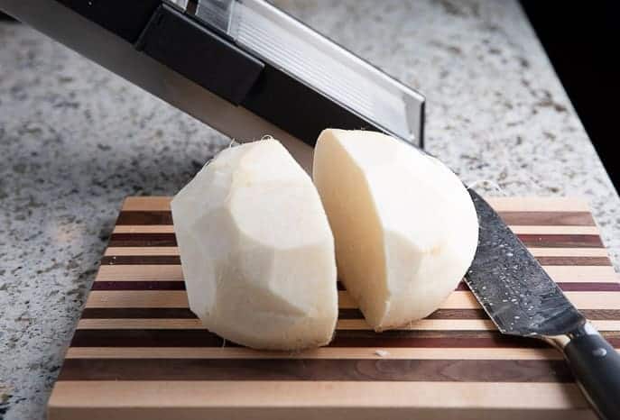 Jicama cut in half on a cutting board with knife and mandoline in the background