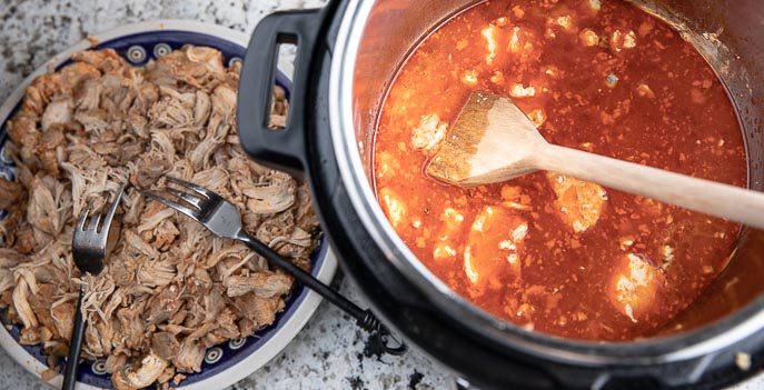 shredded chicken on a plate with fork, sauce in Instant Pot with wooden spoon