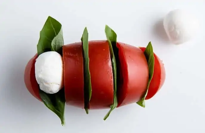 Roma tomato sliced with basil leaves in between slices and one mozzarella pearl