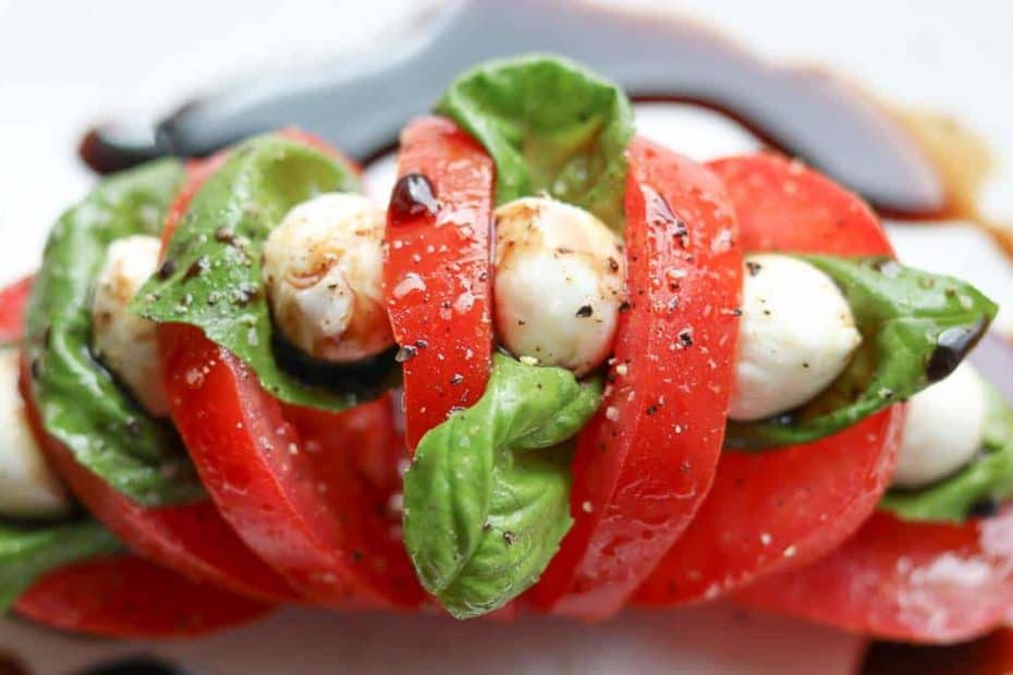 tomato sliced hasselback style on a white plate with basil, mozzarella and balsamic vinegar