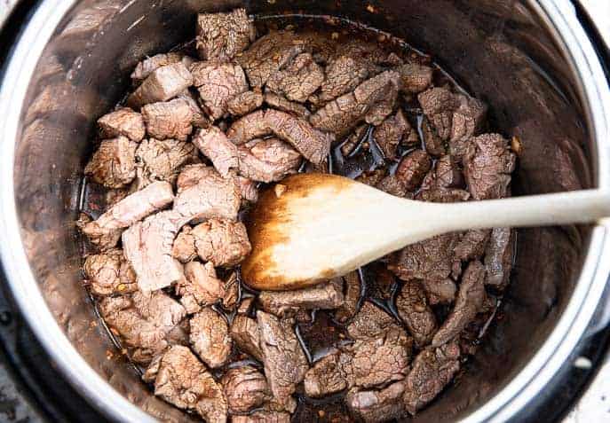 flank steak and soy sauce mixture in Instant Pot with wooden spoon