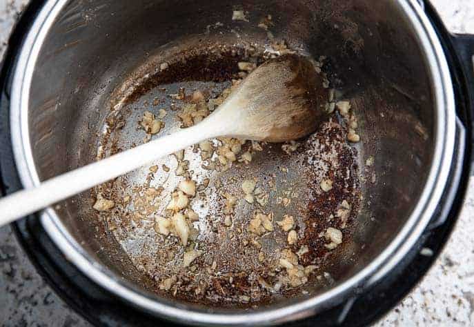 garlic and ginger browning in Instant Pot with wooden spoon