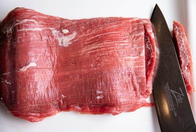 flank steak on a white cutting board with knife