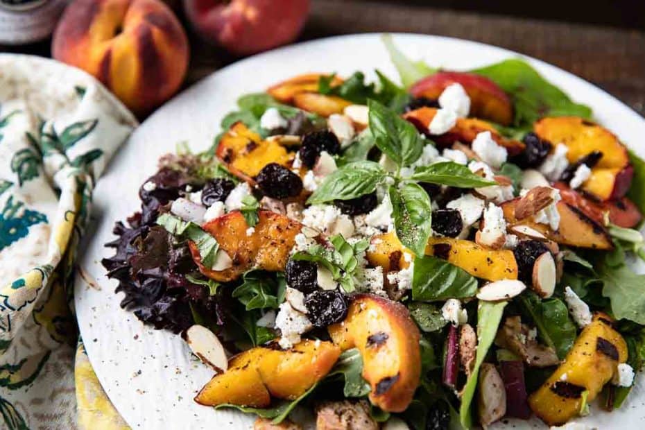 Grilled peach salad - Salad greens with peaches, chicken, goat cheese, basil, dried cherries on a white plate with peach and colored napkin in background
