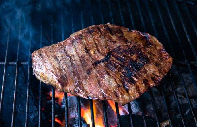 flank steak on a grill with red coals