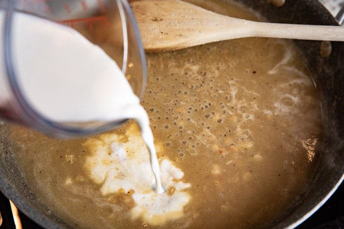 Parmesan Sauce in a pan with half and half being poured and wooden spoon