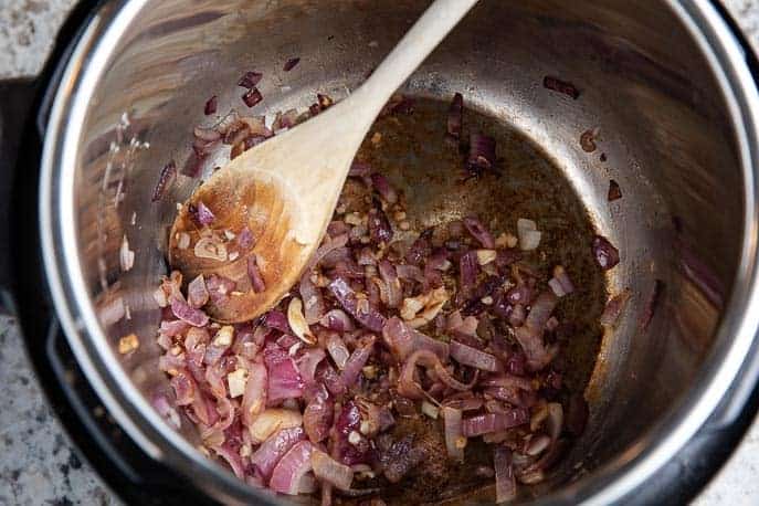 red onions browning in Instant Pot with wooden spoon on granite counter