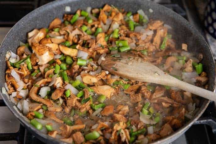 skillet with mushrooms, asparagus, onion and herbs with a wooden spoon
