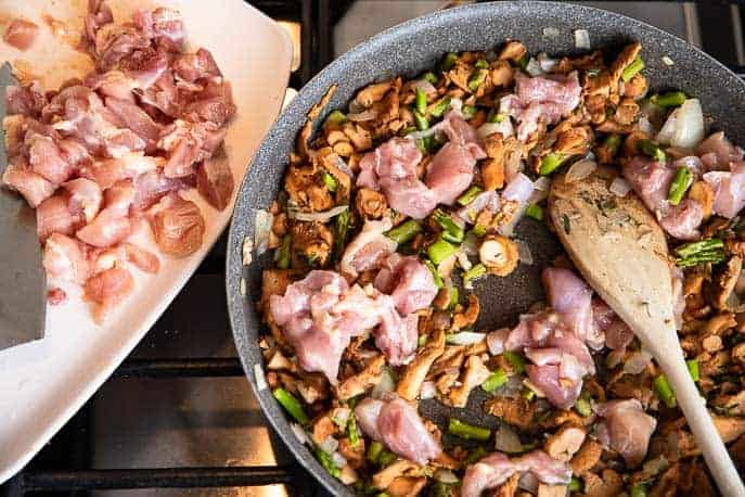 raw chicken pieces in vegetables in a skillet with wooden spoon