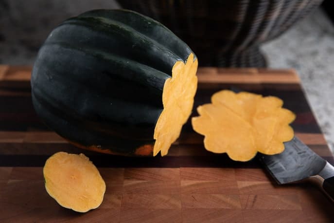 acorn squash with ends cut off on a wooden cutting board with knife