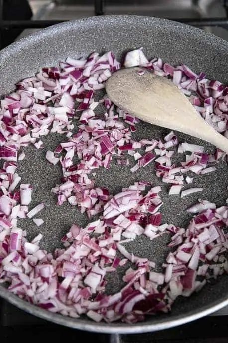 chopped red onions in a non stick pan with wooden spoon