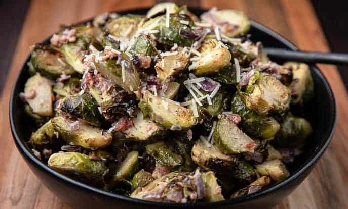 Roasted Brussels Sprouts in Creamy Parmesan Sauce in a black bowl on a wooden board with spoon