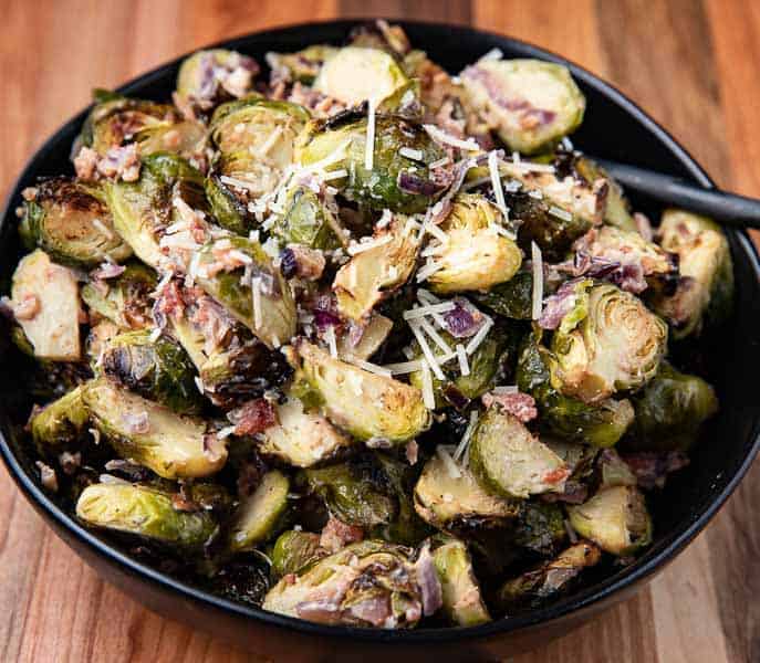 Roasted Brussels Sprouts in Creamy Parmesan Sauce in a black bowl on a wooden board with spoon