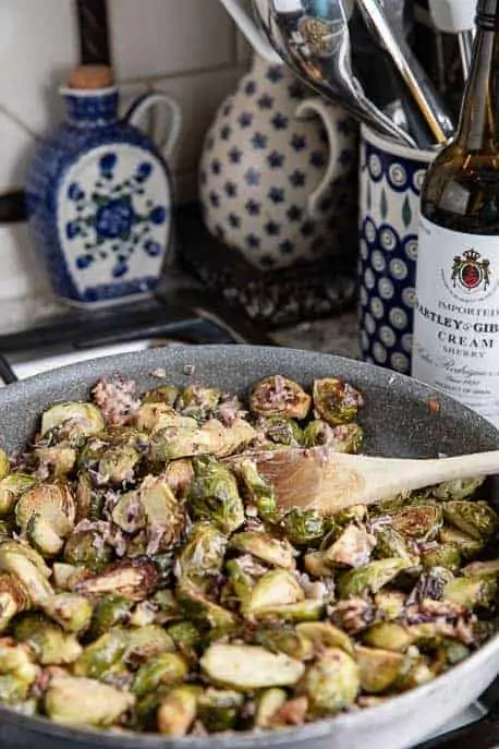 pan of roasted brussels sprouts in parmesan sauce with sherry and Polish pottery in the background