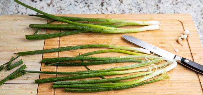 green onions on a wooden cutting board with knife