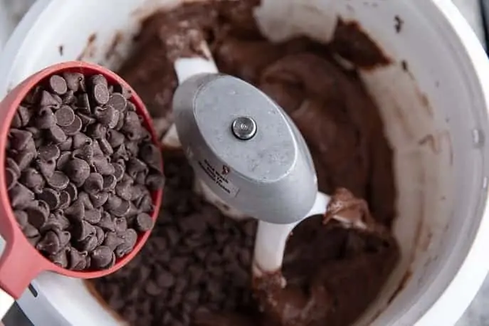 Artiste mixer bowl with cookie batter, chocolate chips in measuring cup pouring in