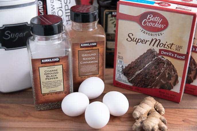 Ingredients for Spicy Chocolate Snaps on a wooden board - eggs, pepper, ginger, cake mix, cinnamon, sugar