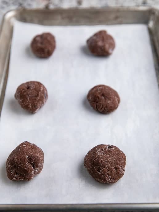 6 Chocolate Snap cookie dough balls on parchment paper on a baking sheet ready to be baked