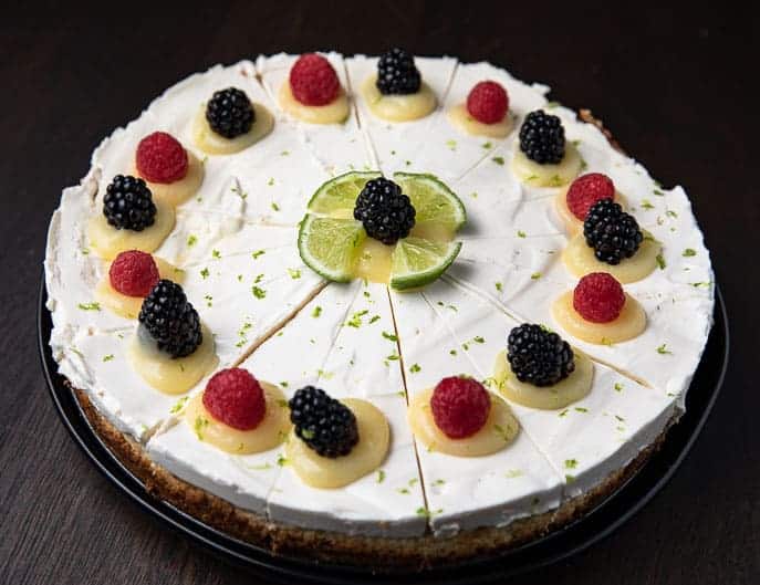 Best Cheesecake in the World on a black plate decorated with lime curd, lime zest, blackberries and raspberries