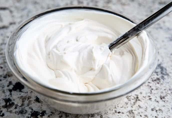 sour cream topping for cheesecake in a glass bowl with a spoon