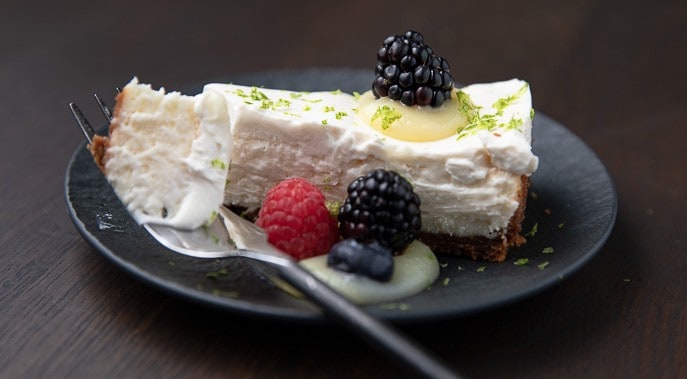 cheesecake on a black plate with blackberries, raspberry and lime curd, lime zest