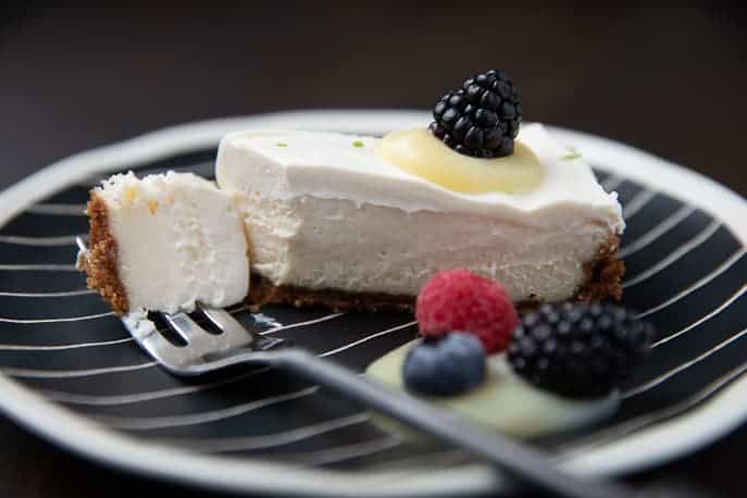 cheesecake with lime curd, blackberries on a striped black and white plate with fork
