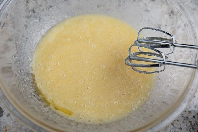 eggs, melted butter and lime juice in a glass bowl with hand mixer on a granite countertop