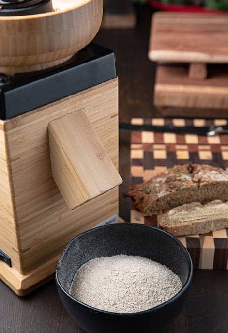 Flour grinder, board with sliced bread, black bowl with freshly ground flour
