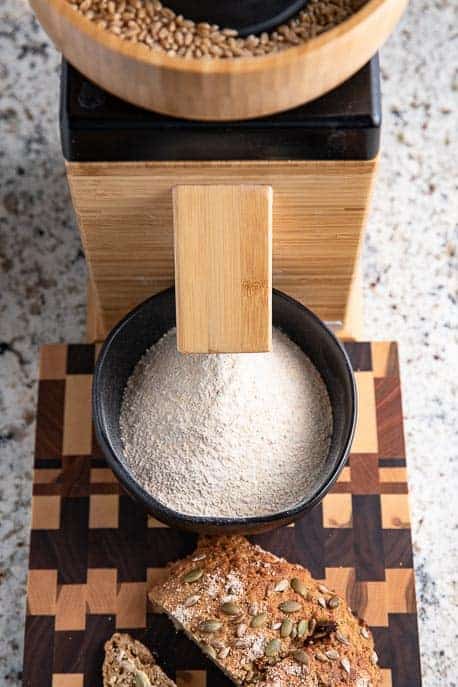 Flour grinder, board with sliced bread, black bowl with freshly ground flour