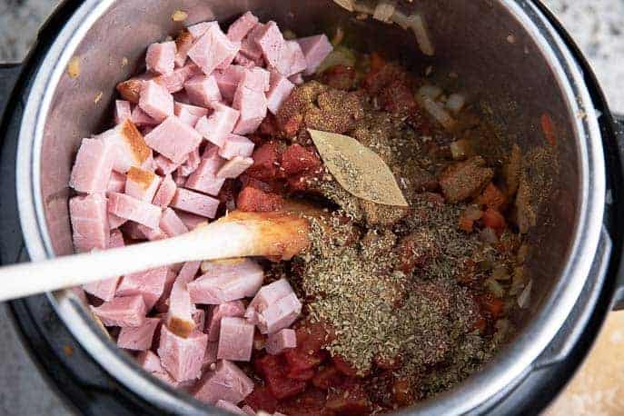 ham, spices, bay leaf, tomato in an Instant Pot with wooden spoon