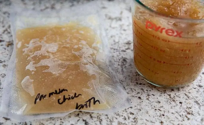 Parmesan chicken broth in a vacuum sealed bag, next to a glass measuring cup with broth